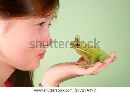 Teenage girl kissing Tree frog (Litoria infrafrenata) with a crown on his head