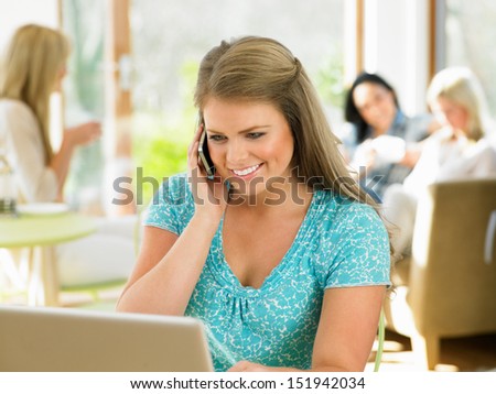 Woman Using Mobile Phone And Laptop In Cafe