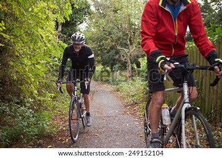 Two Mature Male Cyclists Riding Bikes Along Path