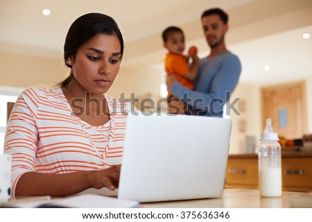 Family In Kitchen With Mother Using Laptop At Table