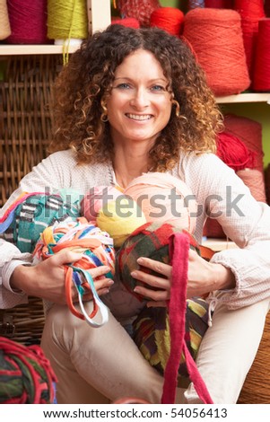 Woman Holding Balls Of Wool Sitting In Front Of Yarn Display