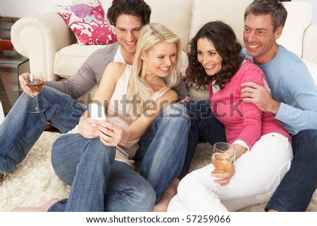 Group Of  Friends Looking At Pictures On Smartphone At Home