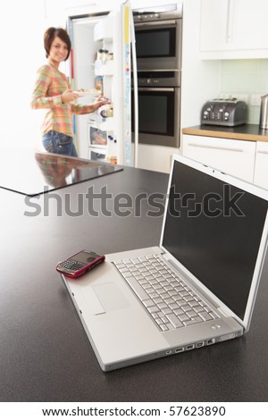 Young Woman Fixing Snack In Kitchen With Laptop In Modern Kitchen