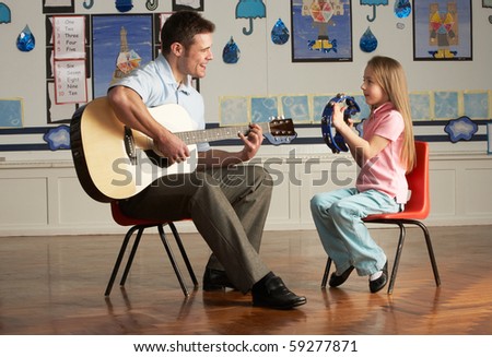 Male Teacher Playing Guitar With Pupil In Classroom