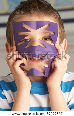 Male Primary School Pupil Cutting Out Paper Shapes In Craft Lesson