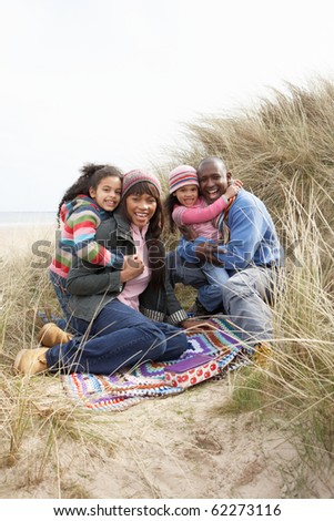 Family Sitting On Blanket In Dunes On Winter Beach