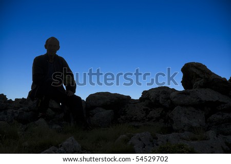A man sitting on a top of the mountain watching the sunset