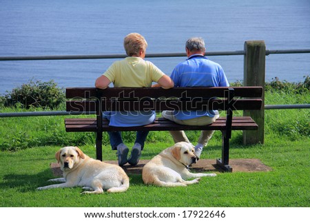 A couple relaxing looking out to sea whilst their dogs look the other way
