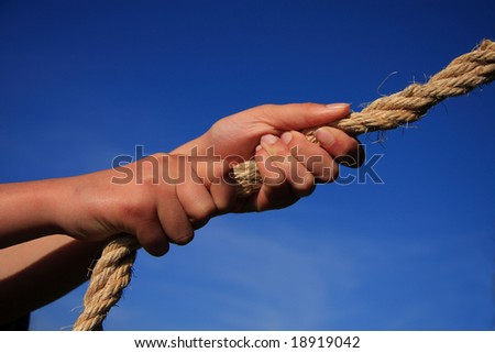 Conceptual image - hands pulling on a rope blue sky background. Might signify strength pulling power determination teamwork etc.