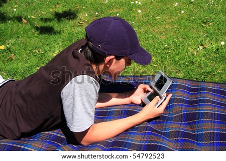 A boy relaxing in the garden playing with his console game