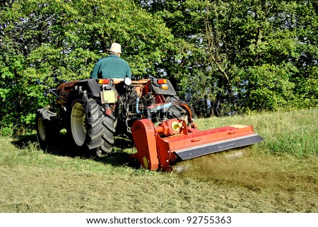 Small farm tractor bush hogging on a grass field in Trentino Alto Adige. Italy