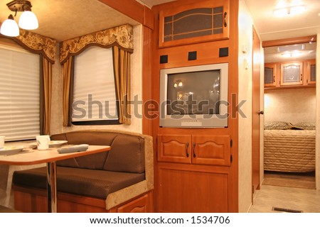 interior of motor home with dining table and dishes, tv, covered windows, and bedroom showing