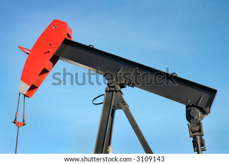 close up view of a black and red oil pump jack against blue sky