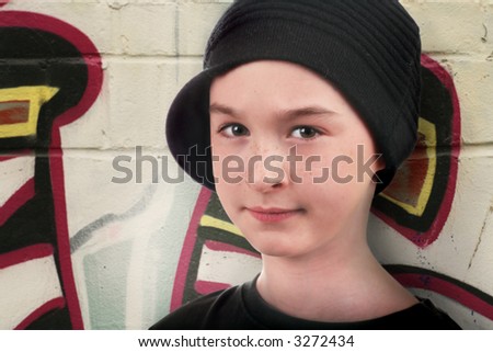 a kid in the street standing against a wall with graffiti and trying to look tough
