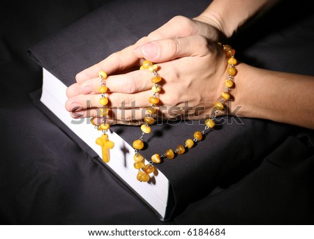 adult woman\'s hands in the dark praying beads over the Holy Bible