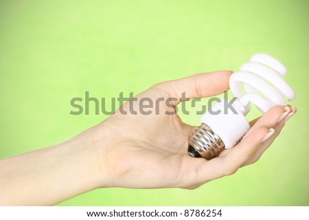 female hand holding a compact fluorescent energy saving environment friendly bulb on green background