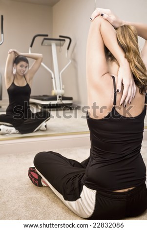A young woman stretching in front of a gym mirror