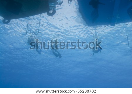 Underwater view of three scuba diver silhouettes at the back of their dive boat. Temple, Sharm el Sheikh, Red Sea, Egypt.
