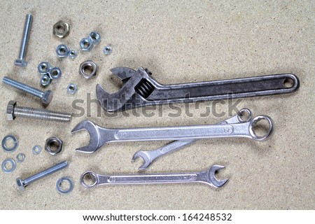 Wrench, monkey wrench and various bolts and nuts on particle board.
