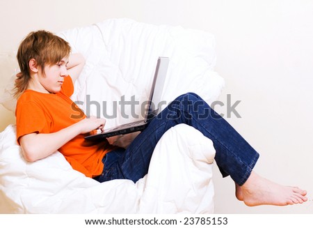 The teenager in an orange t-short works with a laptop in an armchair