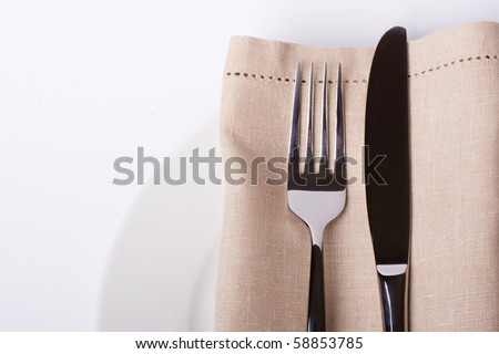 A place setting with silver fork and spoon, white dinner napkin, and white china plat