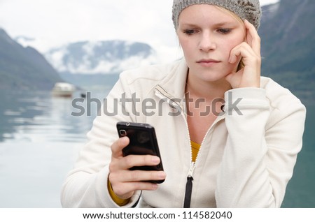 have young blond woman with her Smartphone in the hand and a fjord in Norway in the background