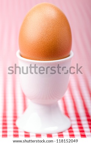 a breakfastt egg in a eggcup on red checked table cover