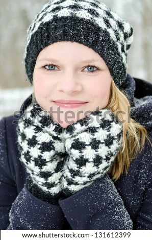 young blond woman smiles with checked beanie and checked scarf in the winter wood