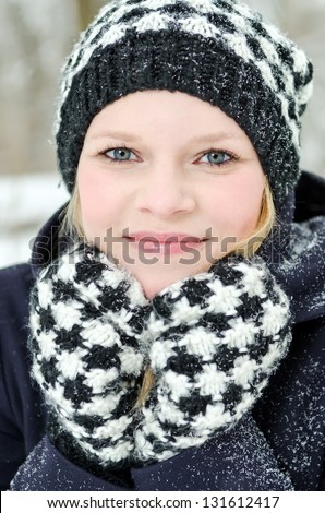 young blond woman smiles with checked beanie and checked scarf in the winter wood
