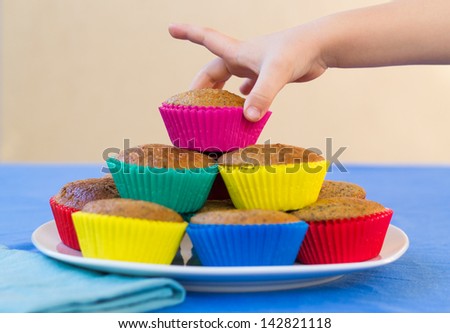Plate of colourful, home-made muffins for a children\'s party, with a child\'s hand reaching for a muffin.