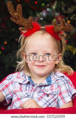 Adorable child eating Christmas lunch wearing reindeer antlers. Christmas tree lights in soft focus in background.