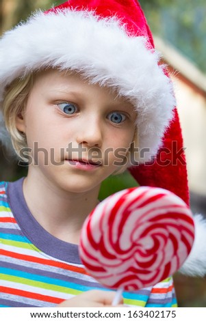 Cute child in Santa hat starring cross-eyed at at a Christmas large lollipop