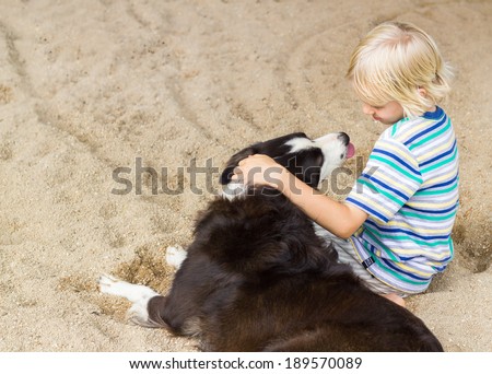 Young boy sitting with arm around his pet dog at the beach