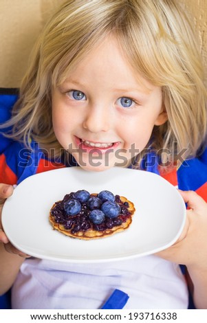 Adorable child holding a healthy homemade wholemeal pikelet with fresh blueberries and jam on top