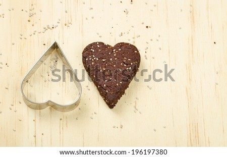 Dark chocolate chia seed love heart cookie and cookie cutter on wooden background