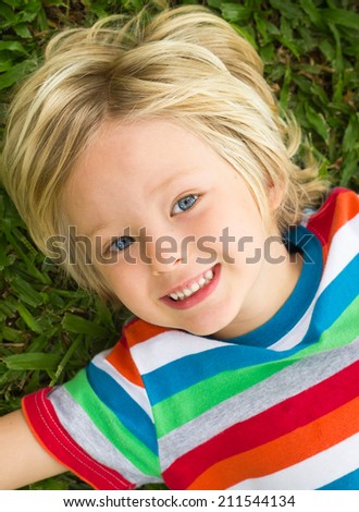 Cute happy child in colorful t-shirt lying on grass