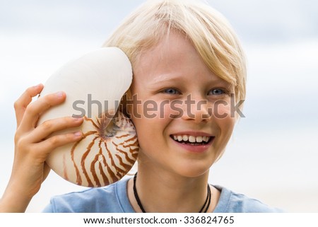 Cute, happy child holding nautilus shell to ear at the beach