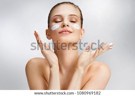Beautiful woman applying moisturizing cream on her face. Photo of woman with flawless skin on grey background. Skin care and beauty concept