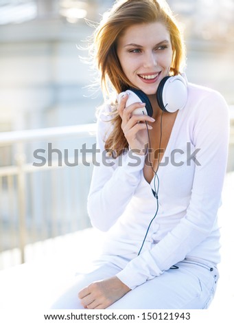 Delightful young woman holds the headphones / smiling brunette girl in a bright clothing with white headphones looking to the side