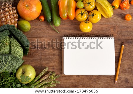 Purchase list. Space for text / studio photography of open blank ring bound notebook surrounded by a fresh vegetables and pencil on old wooden table
