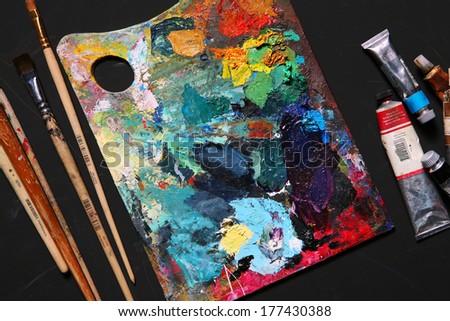 Painting brushes and palette with oil paint / studio photography of paint utensils on black background