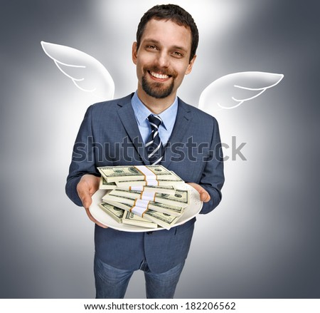 Business angel with money / happy smiling young businessman in a suit jacket offering stacks of US dollar bills - isolated on gray background