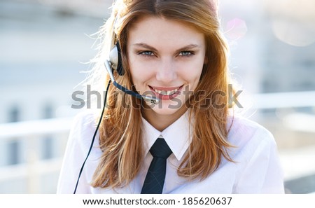 Busy call center agent speaking hands free / smiling brunette girl in a shirt with a tie using handsfree