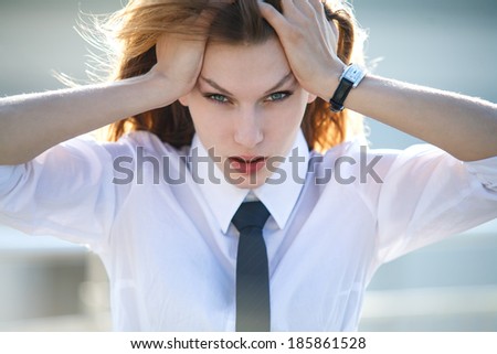 Distressed young woman holds her head with both hands / unhappy brunette girl in a shirt and tie holding her head with both hands