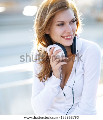 Enchanting young woman holds the headphones / smiling brunette girl in white clothes with white headphones looking to the side