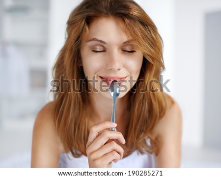 Pleasure from eating / portrait of young smiling woman with spoon in her mouth