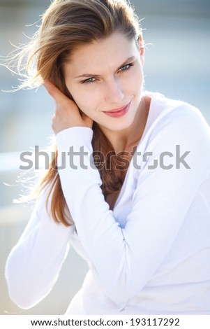 Beautiful woman touches her hair / brunette smiling girl wearing white sweater, straightening her hair