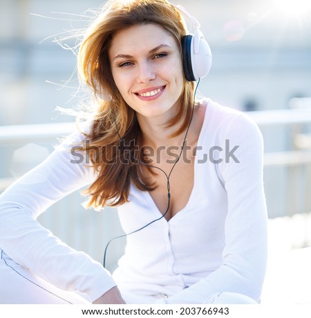 smiling brunette girl  in white clothes with white headphones looking at you