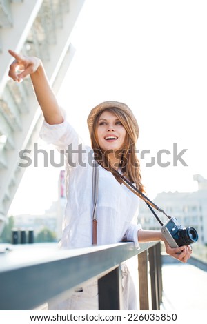 Travel tourist woman with camera pointing up with her finger / photography of young Caucasian woman outdoors