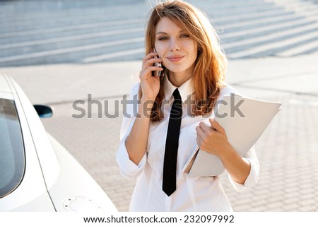 Successful businesswoman or entrepreneur talking on cellphone while walking outdoor. City business woman working / talkative woman in a white button down shirt with black tie
